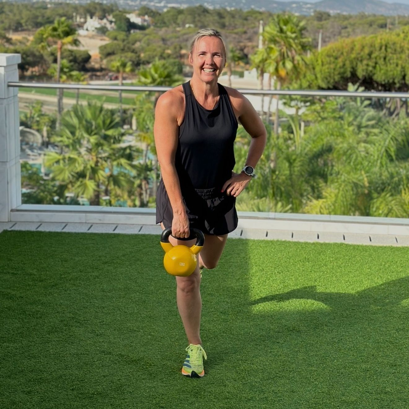 The coach does a lunge outdoors holding a yellow kettlebell.